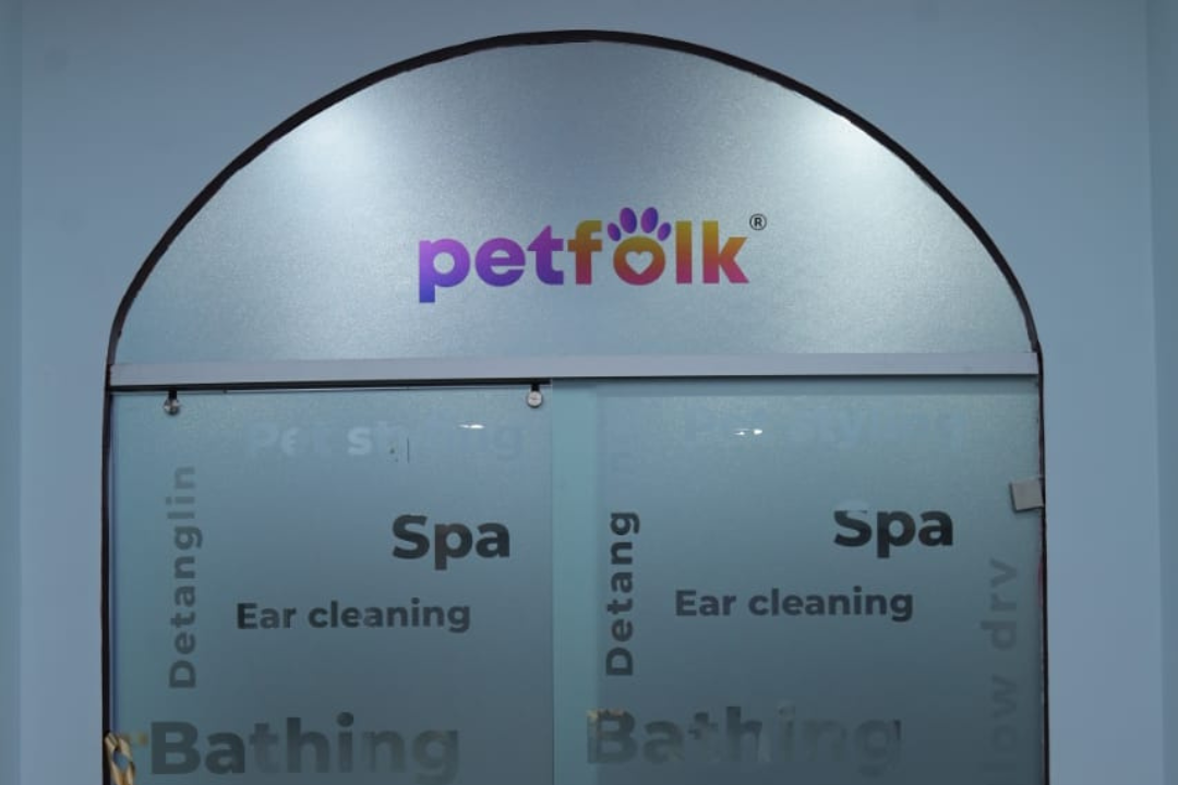 Close-up view of Petfolk signage over a transparent glass panel showcasing services like ear cleaning, spa, and bathing for pets.