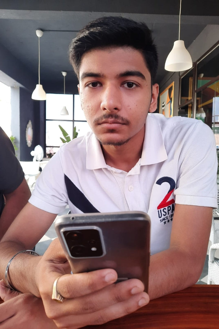 A young man taking a selfie, wearing a polo shirt with a USA logo, in what appears to be a cafe or restaurant setting.